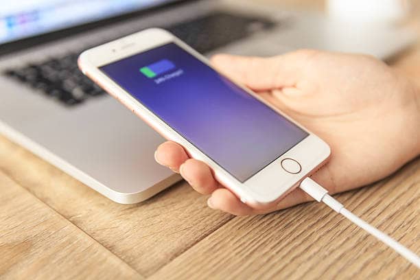 How to Easily transfer photos from your iPhone to a computer 3 Close-up of hands connecting a lightning cable to transfer photos from an iPhone to a USB port on a laptop. Text overlay